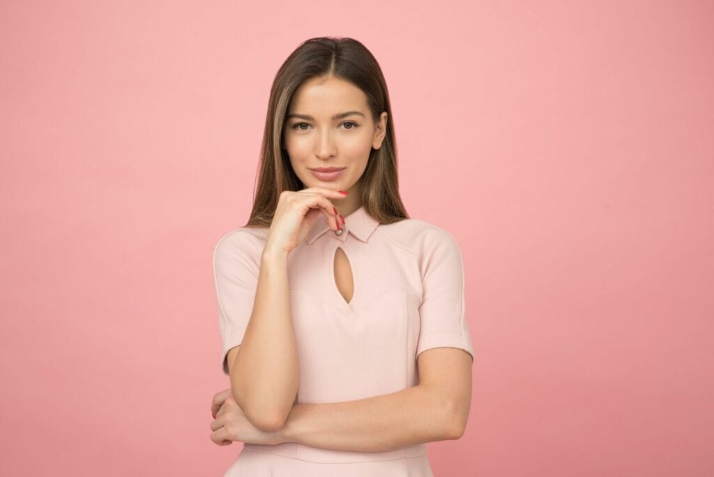 Attractive lady posed in a thinking stance, wearing a lighter pink contrasted by a darker pink background
